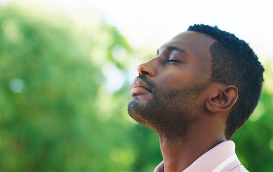 A man enjoys a serene moment in a park, breathing deeply amidst greenery.